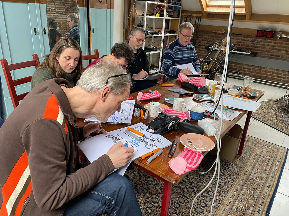 Een groep mensen tekent aan een tafel met papier, stiften en etuis.