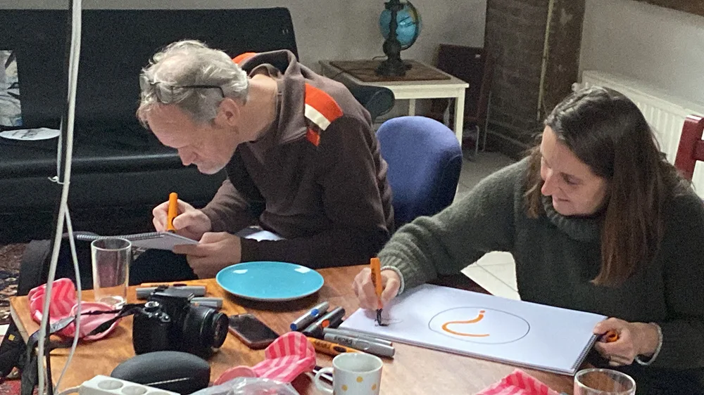 Twee deelnemers werken met stiften aan tekeningen tijdens een workshop.